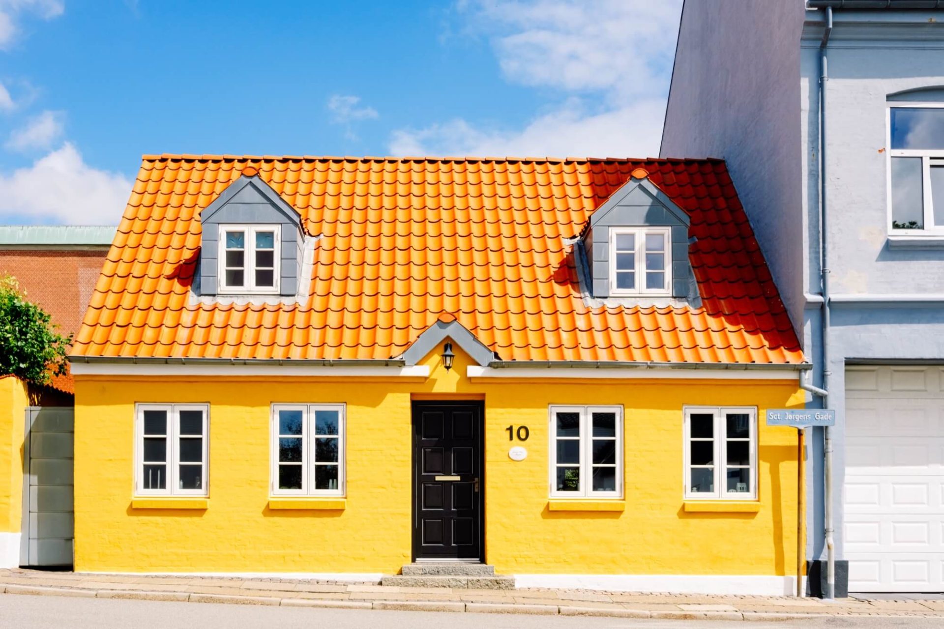 Mitt i staden reser sig ett hus klätt i gult, med ett distinkt orange tak och mörka dörrar